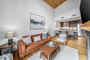 Ein modernes Wohnzimmer mit einer braunen Ledersofa, einem Holztisch und einer Küchenzeile mit Edelstahlgeräten.