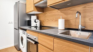 Una cucina moderna con mobili in legno, un frigorifero in acciaio inossidabile, un forno a microonde, una macchina da caffè, una lavatrice e un lavello con rubinetto.