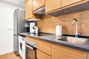A modern kitchen with wooden cabinets, a stainless steel refrigerator, a microwave, a coffee maker, a washing machine, and a sink with a faucet. - Sea View Apartment with Terrace - Horizon (La Vila Joiosa)