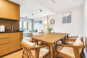 A modern kitchen with wooden cabinets, a dining table with chairs, and a living area with a sofa and a lamp. - Sea View Apartment with Terrace - Horizon (La Vila Joiosa)
