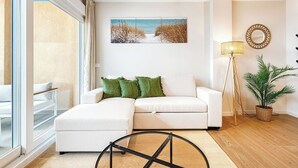 Un soggiorno moderno con un divano bianco, una lampada da terra, una pianta in vaso e un quadro raffigurante una spiaggia.