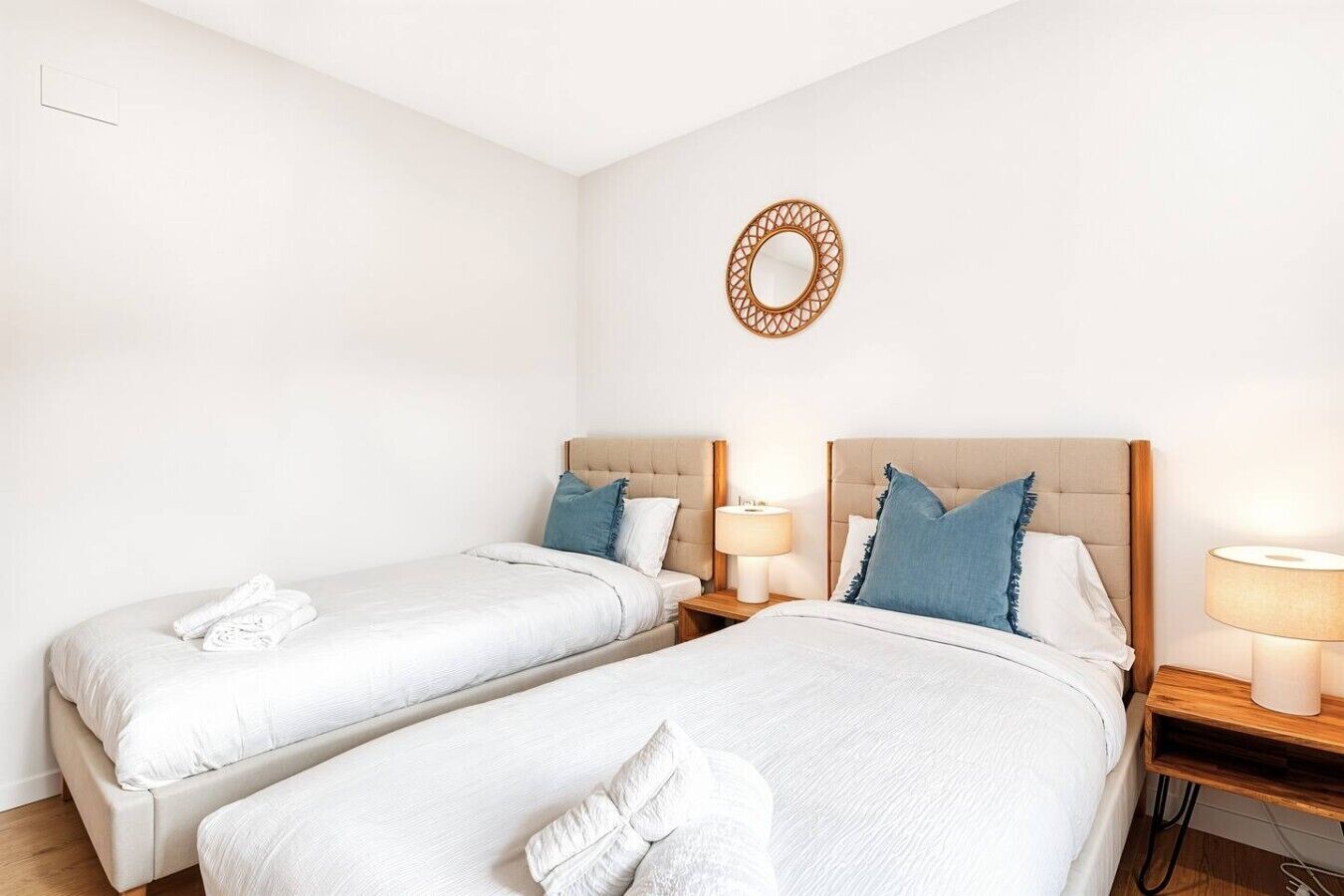 A hotel room with two beds, each with a pillow and a bedside table with a lamp.