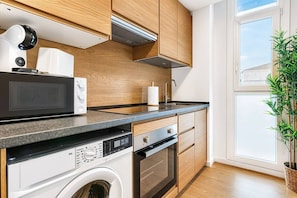 A modern kitchen with wooden cabinets, a microwave, a washing machine, and a large window. - Sea View Apartment with Terrace - Sunset (La Vila Joiosa)