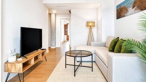 Un salon moderne avec un téléviseur à écran plat, une table basse en bois, un canapé blanc et un lampadaire.