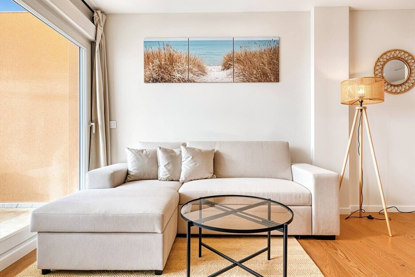 Een moderne woonkamer met een bank, een glazen salontafel, een vloerlamp en een kunstwerk met een strandthema aan de muur.