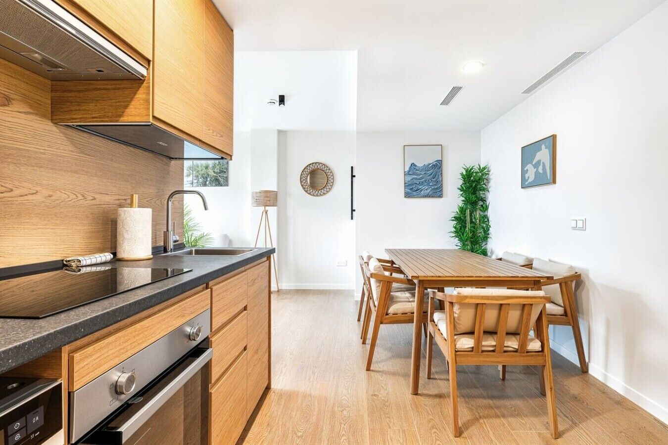 Een moderne keuken met houten kasten, een roestvrijstalen fornuis en een eethoek met een houten tafel en stoelen.
