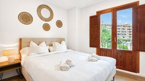 Um quarto com cama, almofadas, mesa de cabeceira com abajur e janela com persianas de madeira.