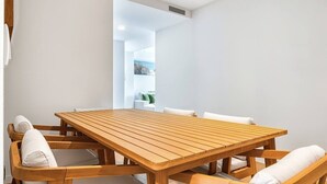 Una mesa de comedor de madera con sillas blancas acolchadas, una pared blanca y una puerta visible que da a otra habitación.