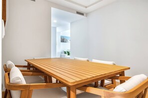 A wooden dining table with white cushioned chairs, a white wall, and a visible door leading to another room. - Sea View Apartment with Terrace - Breeze (La Vila Joiosa)