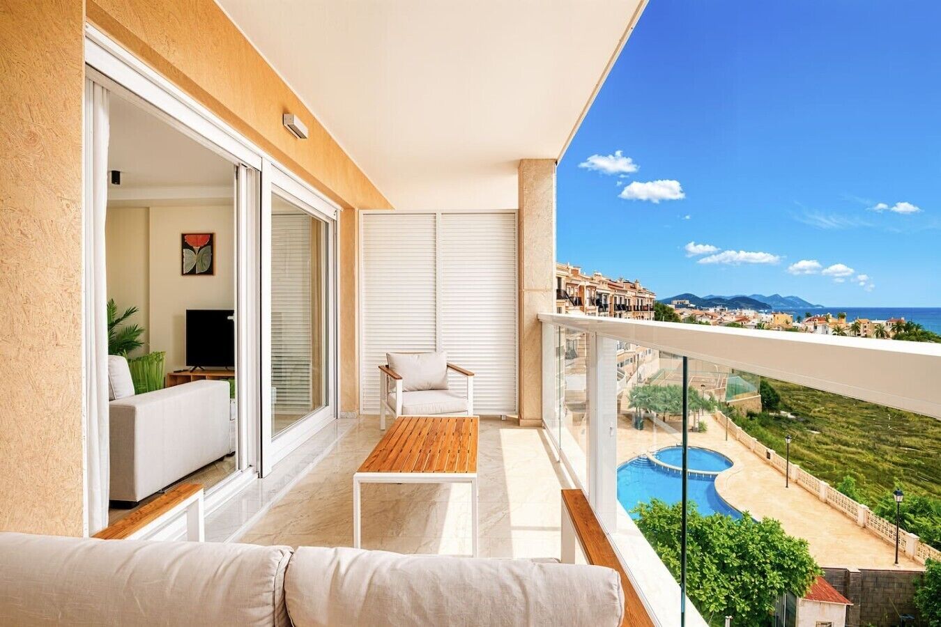 A balcony with a sofa, a table, and a view of a swimming pool and buildings.