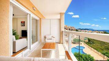 A balcony with a sofa, a table, and a view of a swimming pool and buildings.