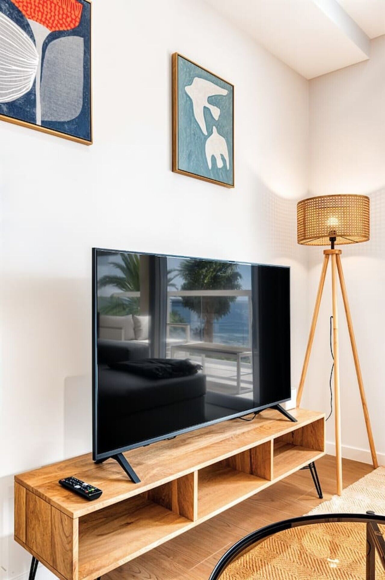 A modern living room with a flat-screen TV on a wooden stand, a floor lamp, and artwork on the wall.