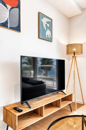 Ein modernes Wohnzimmer mit einem Flachbildfernseher auf einem Holzständer, einer Stehlampe und Kunstwerken an der Wand.