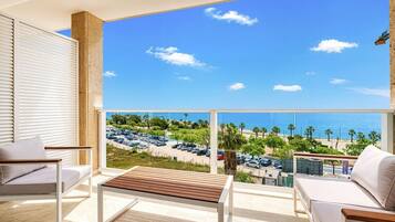 A balcony with a view of the sea, a parking lot, and a building in the background.
