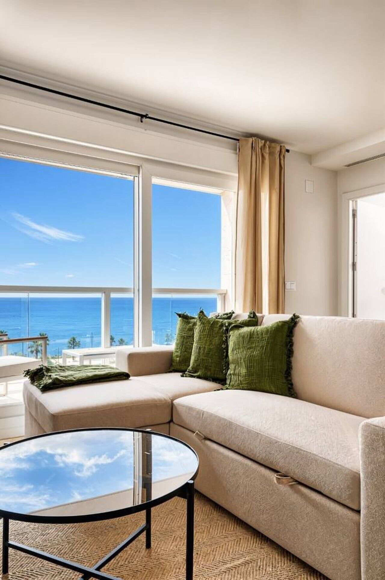 En stue med en beige sofa, et glasbord og havudsigt.