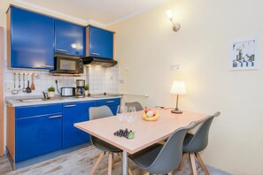 Cozinha compacta com armários azuis, micro-ondas e área de jantar com mesa e cadeiras.
