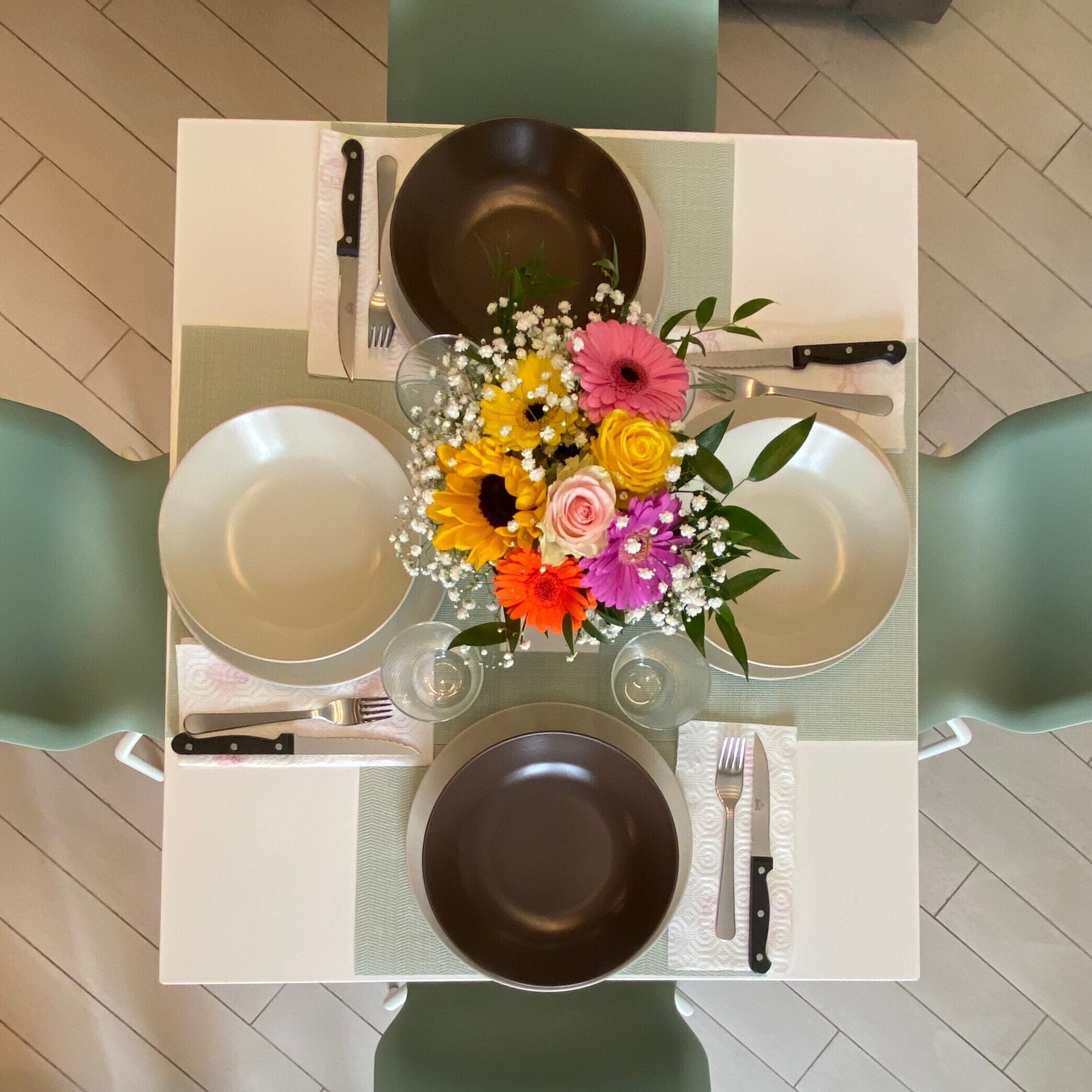 Une table carrée avec quatre assiettes, deux fourchettes, deux couteaux et un vase de fleurs.