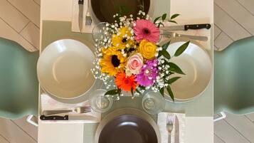 Une table carrée avec quatre assiettes, deux fourchettes, deux couteaux et un vase de fleurs.
