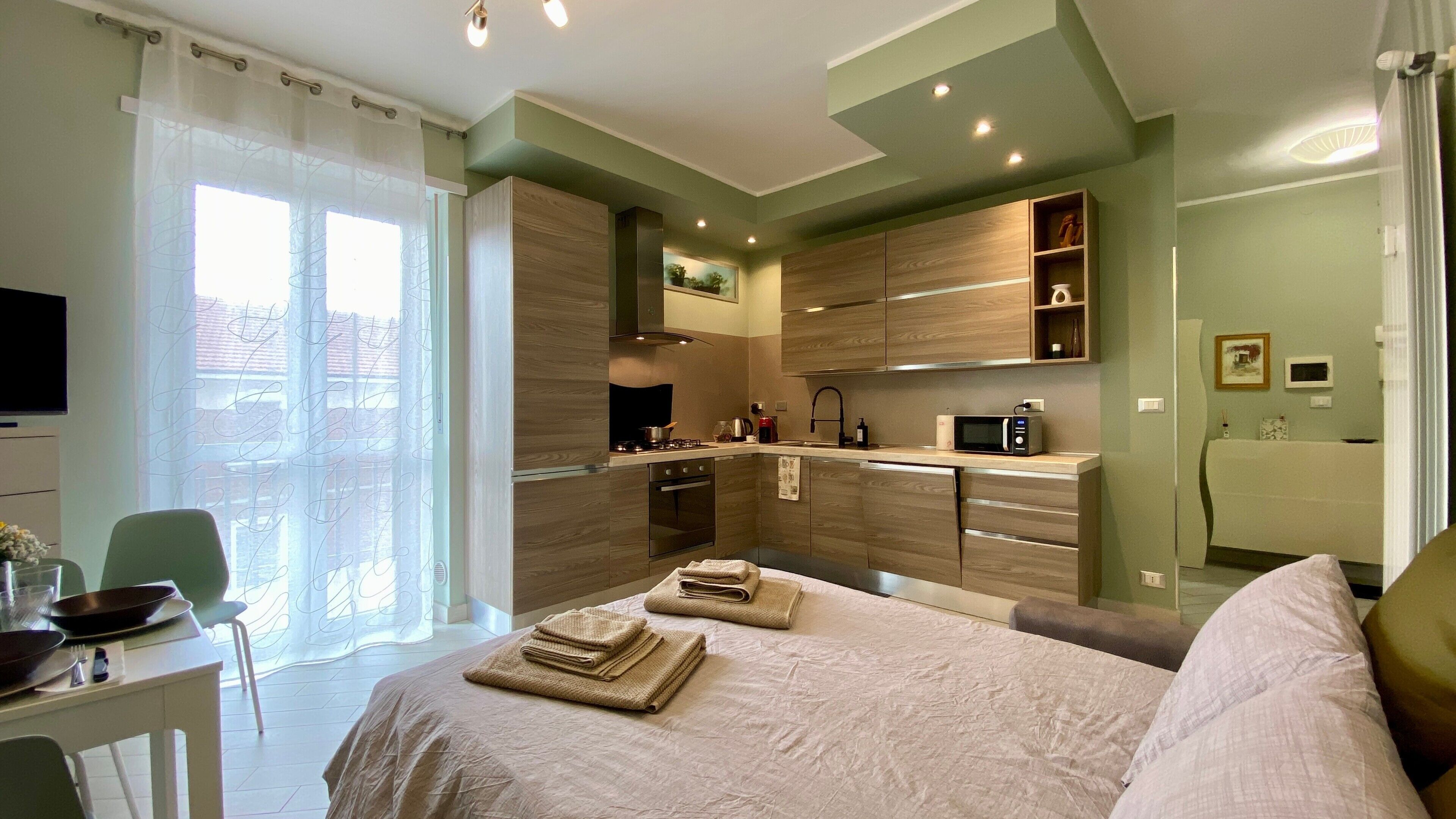 A modern hotel room with a bed, a dining table, a kitchen area, and a TV.. Il Bumbunin di Collegno – Free Parking in Central Location