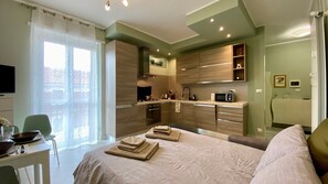 Ein modernes Hotelzimmer mit Bett, Esstisch, Küchenzeile und Fernseher.
