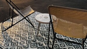 Une terrasse avec un tapis à motifs, une table blanche et deux chaises.