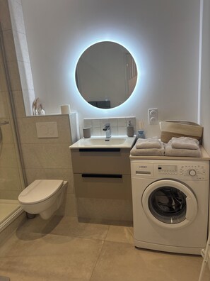 A modern bathroom with a toilet, sink, mirror, and washing machine. - A little haven of peace in the heart of the Basque country (Urcuit)