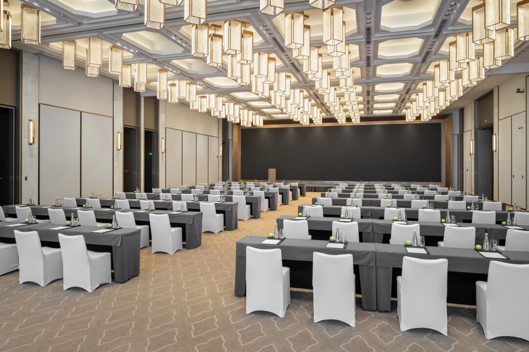Un salón de conferencias con mesas, sillas y una pantalla grande.