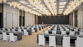 Un salón de conferencias con mesas, sillas y una pantalla grande.