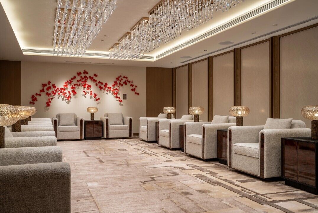 A hotel lobby with a patterned carpet, multiple seating areas, and a decorative wall with red flowers.