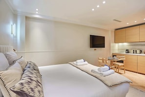 Ein Hotelzimmer mit Bett, Schreibtisch, Stuhl, Flachbildfernseher und einer Küchenzeile.