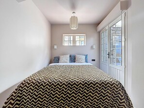 Een slaapkamer met een bed met een patroondisign, een kroonluchter, een raam met uitzicht en een deur.
