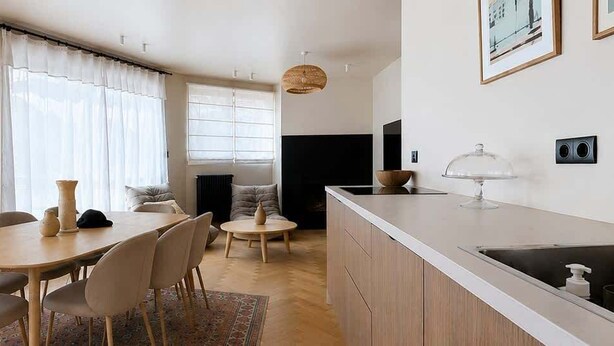 Eine moderne Küche mit weißer Arbeitsplatte, Spüle aus Edelstahl und einem Essbereich mit Holztisch und Stühlen.