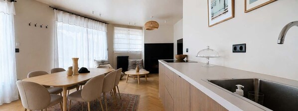 Een moderne keuken met een wit aanrecht, een roestvrijstalen spoelbak en een eethoek met een houten tafel en stoelen.