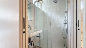 Ein modernes Badezimmer mit einer Duschkabine, einem weißen Waschbecken und einem Spiegel.