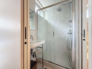 Een moderne badkamer met een douchecabine van glas, een wit wastafelmeubel en een spiegel.