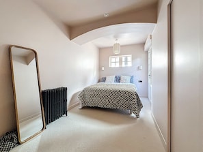 Een slaapkamer met een bed, spiegel, radiator en raam.