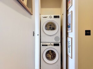 A laundry room with two stacked Bosch washing machines, a door, and a wall-mounted light switch. - Spacious flat in the heart of Deauville (Deauville)