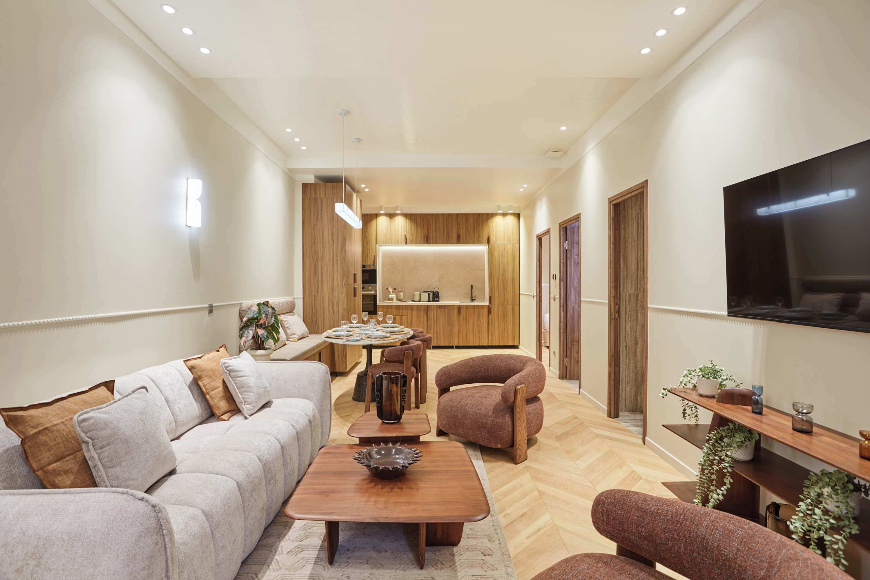 Una sala de estar moderna con un sofá, un sillón, una mesa de centro y un televisor montado en la pared.