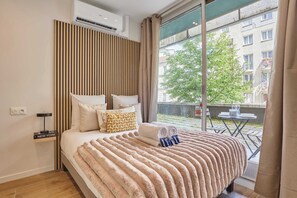Ein modernes Hotelzimmer mit einem großen Bett, Blick auf die Stadt und einem Balkon mit Gartenmöbeln.