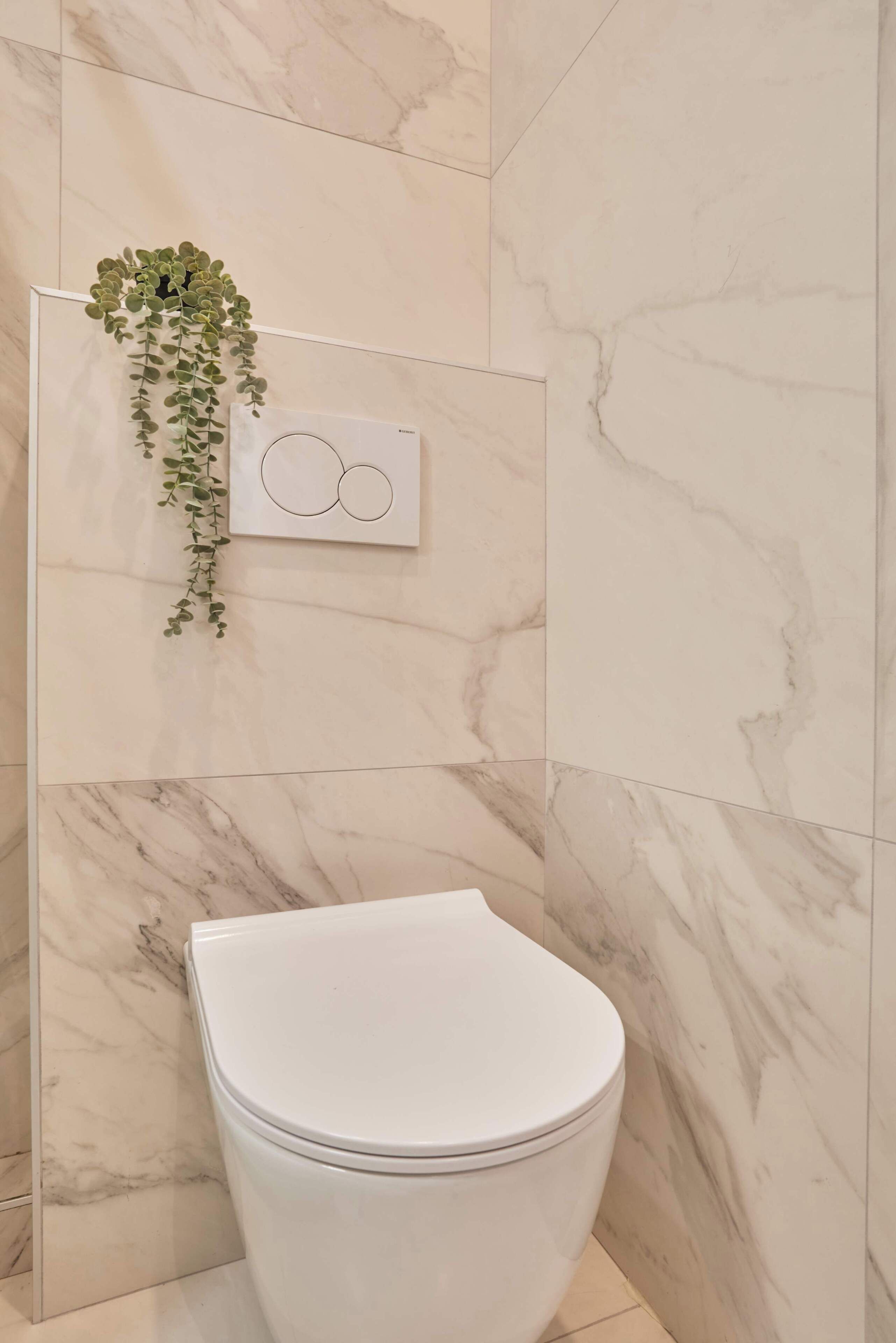 A bathroom with a toilet, marble walls, and a hanging plant.