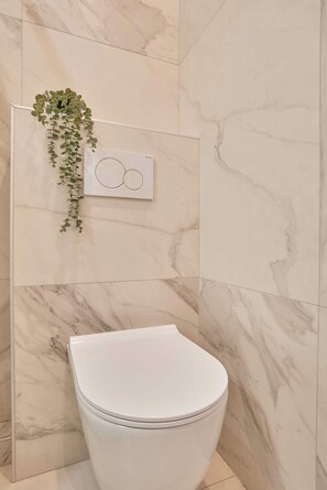 Ein Badezimmer mit Toilette, Marmorwänden und einer hängenden Pflanze.
