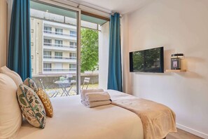 A hotel room with a bed, a TV, and a view of a building and trees. - Suite with balcony & AC -Eiffel Tower-Beaugrenelle (Paris)