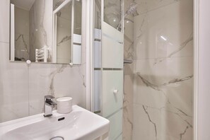A bathroom with a white sink, a mirror, and a shower area with glass doors. - Suite with balcony & AC -Eiffel Tower-Beaugrenelle (Paris)