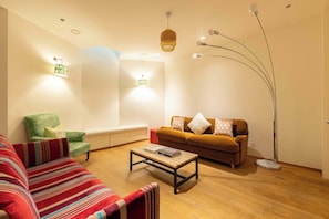 Ein Wohnzimmer mit Sofa, Sessel, Couchtisch, Stehlampe und Wandleuchten.