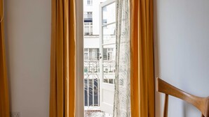 Vista attraverso una finestra con tende gialle, una sedia di legno e un edificio sullo sfondo.