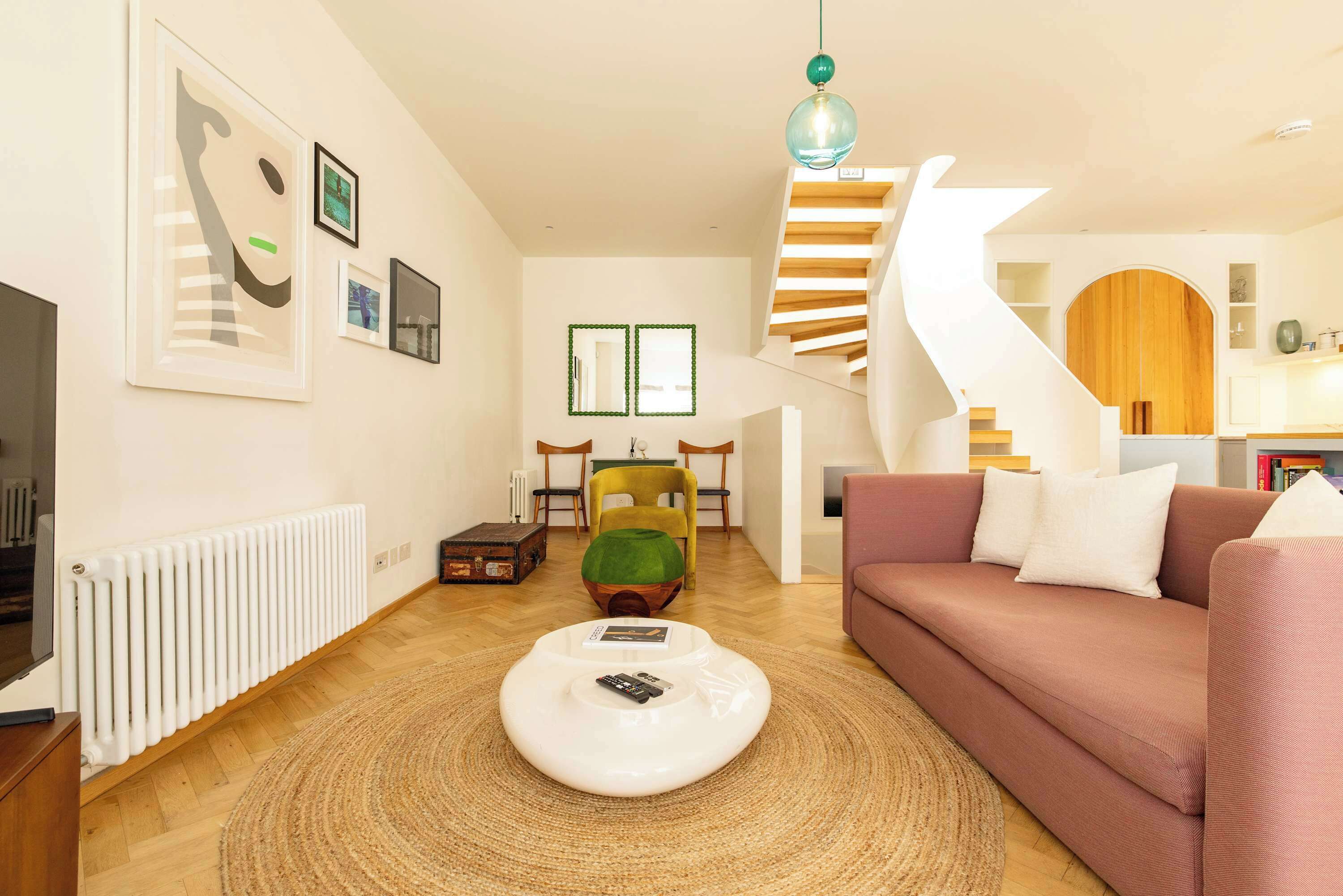 A modern living room with a sofa, a coffee table, a staircase, and a dining area.