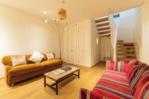 A living room with a sofa, a coffee table, and a staircase. - South Kensington - Mews House, Sleeps 6 (Greater London)