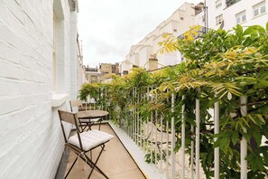 A narrow outdoor corridor with a white wall on one side, a small table with chairs, and a climbing plant supported by white poles. - South Kensington - Mews House, Sleeps 6 (Greater London)