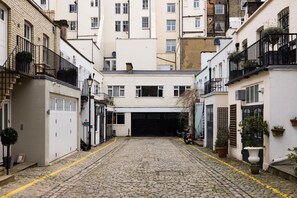 Une ruelle étroite pavée, bordée de bâtiments aux façades blanches, avec une porte de garage et des plantes en pot.
