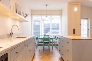 A modern kitchen with a central island, a built-in sink, and a dining area with chairs. - South Kensington - Mews House, Sleeps 6 (Greater London)